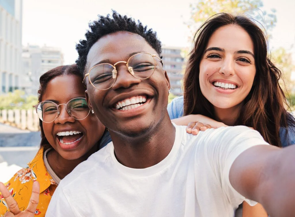 Three smiling students taking a selfie together outdoors