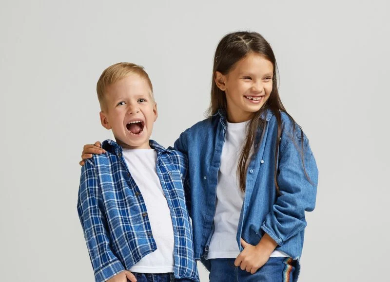 A smiling boy and girl in denim and plaid standing arm in arm